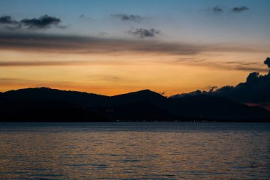 Deniz manzaralı, dağların üzerinde gün batımı.