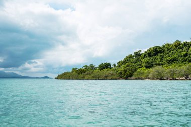 Kristal berrak mavi deniz suyu ve bulutlu gökyüzü olan tropikal bir ada..