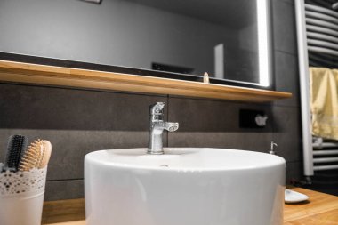 Banyo içi duvarında gri fayans, şık yuvarlak lavabo ve meşe ağacından bir atölyeye musluk. Banyonun içinde minimalizm.