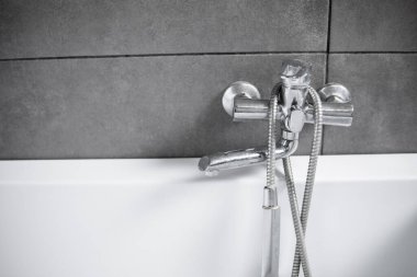 Banyodaki gri fayanslı beyaz banyolu krom musluk. Gümüş musluğu olan şık beyaz bir banyo. Banyonun içinde minimalizm.