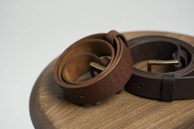 Tahta koltukta bronz tokalı iki kahverengi deri erkek kemeri ve beyaz bir arka plan. El yapımı deri kemer..