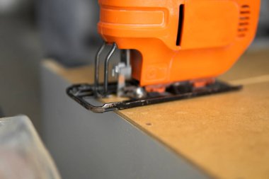 Özel mutfak dolabının arkasındaki fiberboard 'u kesmek için elektrikli yapboz kullanan bir adam eli. Mutfak kurulumu. Profesyonel el testereli bir marangoz..