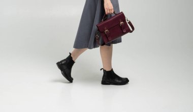 Beyaz arka planda bir kadının elinde küçük kırmızı deri bir çanta. Omuz çantası. Beyaz gömlekli, gri etekli ve kırmızı çantalı bir kadın. Tarz, retro, moda, klasik ve zarafet.