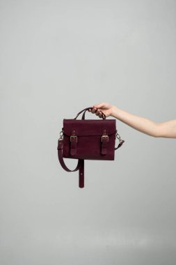 Beyaz arka planda bir kadının elinde küçük kırmızı deri bir çanta. Omuz çantası. Tarz, retro, moda, klasik ve zarafet.