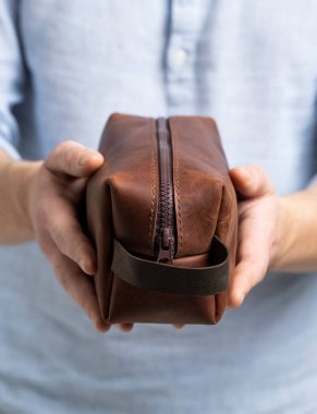 Mans kahverengi deri kişisel makyaj çantası ya da tuvalet malzemeleri için kese mavi gömlekli bir adamın elinde. Tarz, retro, moda, klasik ve zarafet.