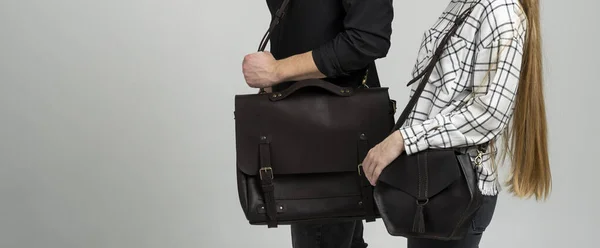 Brown mens shoulder leather bag for a documents and laptop holds by man in a black shirt and woman with a black small bag. Style, retro, fashion, vintage and elegance.