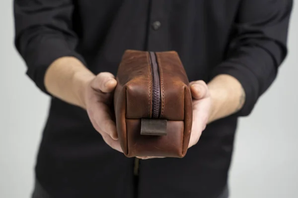 Mans brown leather personal cosmetic bag or pouch for toiletry accessory in a mens hands in black shirt. Style, retro, fashion, vintage and elegance. — Stock Photo, Image