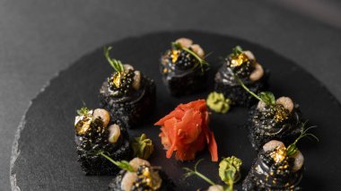 Suşi, siyah pirinç, yengeç eti, salatalık, avokado, tütsülenmiş somon balığı, kürek havyarı, masago, karides kokteyli ve kırmızı zencefil ve wasabi soslu yenilebilir altın yaprak..