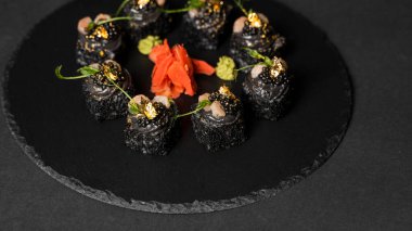 Suşi, siyah pirinç, yengeç eti, salatalık, avokado, tütsülenmiş somon balığı, kürek havyarı, masago, karides kokteyli ve kırmızı zencefil ve wasabi soslu yenilebilir altın yaprak..