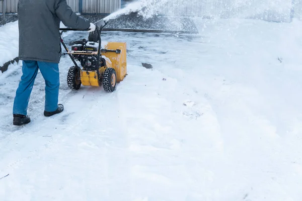 Man cleaning driveway with snow machines after a snow storm. Snow removal equipment working on the street. Cleaning of streets from snow. Its snowing.