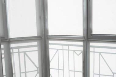 Oturma odasındaki bir balkondaki plastik pencerenin perdeleri beyaz kumaştan..