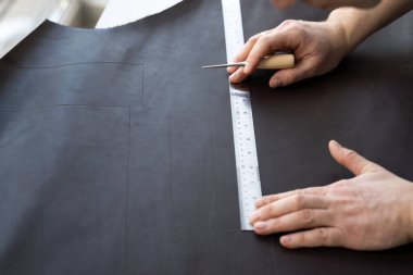 Erkekler bir teneke kutu ve metal cetvel tutuyor ve atölyesinde deri bir cüzdan üzerinde çalışıyorlar. Kahverengi doğal deri ile çalışma süreci. Zanaatkar elinde bir el işi aleti tutuyor ve deriye işaretler koyuyor..