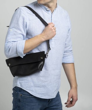 Omzunda deri el yapımı çanta olan mavi gömlekli bir adam. Koyu renk muz torbası. Stüdyodaki adam. Yürümek için rahat bir çanta..