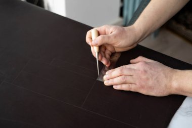 Erkekler bir teneke kutu ve metal cetvel tutuyor ve atölyesinde deri bir cüzdan üzerinde çalışıyorlar. Kahverengi doğal deri ile çalışma süreci. Zanaatkar elinde bir el işi aleti tutuyor ve deriye işaretler koyuyor..