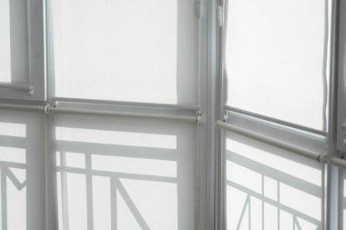 Oturma odasındaki bir balkondaki plastik pencerenin perdeleri beyaz kumaştan..