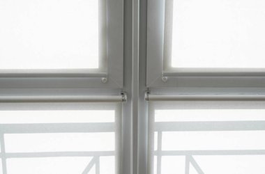 Oturma odasındaki bir balkondaki plastik pencerenin perdeleri beyaz kumaştan..