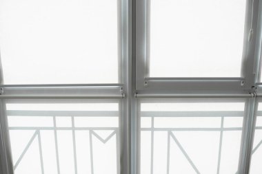 Oturma odasındaki bir balkondaki plastik pencerenin perdeleri beyaz kumaştan..