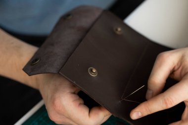 Atölyesindeki deri cüzdan üzerinde çalışan erkekler. Kahverengi doğal deri ile çalışma süreci. Bir zanaatkar elinde zanaat araçları tutuyor..