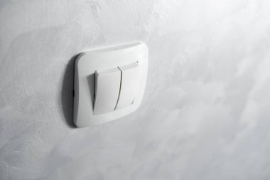 Işık anahtarı, açık gri bir duvara yerleştirilmiş beyaz rengin plastik mekanik anahtarı.