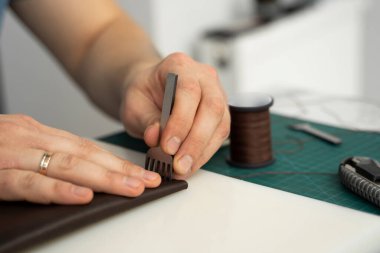 Erkekler deri bir çekiç ve çelik keski ile delik yumruğu tutuyor ve atölyesinde deri bir cüzdan yapıyor. Kahverengi doğal deri ile çalışma süreci. Bir zanaatkar elinde zanaat araçları tutuyor..