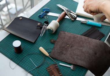 Atölyesindeki deri cüzdan üzerinde çalışan erkekler. Kahverengi doğal deri ile çalışma süreci. Bir zanaatkar elinde zanaat araçları tutuyor..