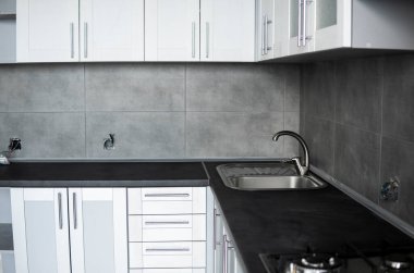 Modern minimalizm stili mutfak iç dekorasyonu tek renkli tonlarda. Mutfak kaputu ve lavabosu olan gri beyaz bir mutfak ve koyu gri bir tezgah. Chipboard 'dan modüler mutfak.