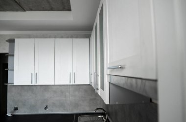 Modern minimalizm stili mutfak iç dekorasyonu tek renkli tonlarda. Mutfak kaputu ve lavabosu olan gri beyaz bir mutfak ve koyu gri bir tezgah. Chipboard 'dan modüler mutfak.