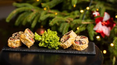 Nori, taze somon, ton balığı, avokado, masago havyarı, ananas sosuyla süslenmiş salata, Noel için ahşap bir masada siyah bir tabağa süsleme olarak serpilmiş özel suşi rulosu..