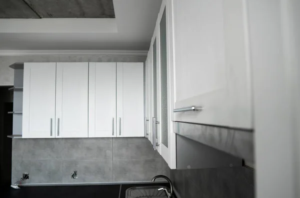 Modern minimalism style kitchen interior in monochrome tones. Custom kitchen with grey white facadesmdf and dark grey countertop with installed kitchen hood and sink. Modular kitchen from chipboard.