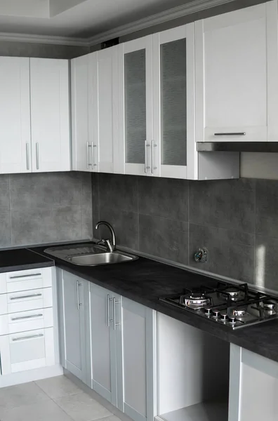 Современный минимализм стиль кухни интерьера в монохромных тонах. Custom kitchen with grey white facadesmdf and dark grey countop with installed kitchen hood and sink. Модульная кухня из ДСП. — стоковое фото