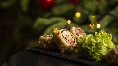 Nori, taze somon, ton balığı, avokado, masago havyarı, ananas sosuyla süslenmiş salata, Noel için ahşap bir masada siyah bir tabağa süsleme olarak serpilmiş özel suşi rulosu..