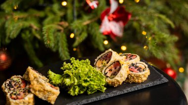 Nori, taze somon, ton balığı, avokado, masago havyarı, ananas sosuyla süslenmiş salata, Noel için ahşap bir masada siyah bir tabağa süsleme olarak serpilmiş özel suşi rulosu..