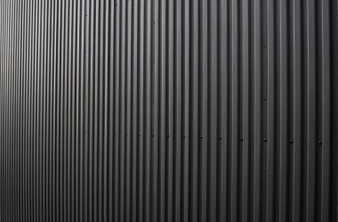 Bir depo ya da fabrika cephesi olarak kullanılan siyah kıvrımlı demir çarşaf. Sivri uçlu çinko kaplamalı metal alüminyum cephenin dokusu. Mimarlık. Metal doku.