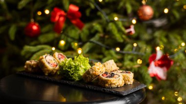 Nori, taze somon, ton balığı, avokado, masago havyarı, ananas sosuyla süslenmiş salata, Noel için ahşap bir masada siyah bir tabağa süsleme olarak serpilmiş özel suşi rulosu..