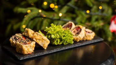 Nori, taze somon, ton balığı, avokado, masago havyarı, ananas sosuyla süslenmiş salata, Noel için ahşap bir masada siyah bir tabağa süsleme olarak serpilmiş özel suşi rulosu..