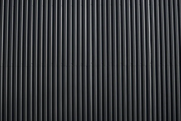 Svart korrugerad järnplåt som används som fasad på ett lager eller fabrik. Konsistens av en sömlös korrugerad zinkplåt aluminium fasad. Arkitektur. Metallstruktur. — Stockfoto