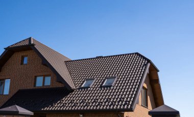 Modern bir eve kahverengi, metal profil çatısı döşenmiş. Çürük çarşafın çatısı. Metal profil dalgalı şeklinin çatısı. Metalden yapılmış modern çatı. Metal çatı..