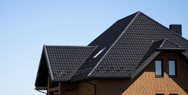 Коричневый гофрированный металлический профиль крыши установлен на современном доме с чердачными окнами. Крыша из гофрированного листа. Крыша металлического профиля волнистой формы. Современная крыша из металла. Металлическая кровля.