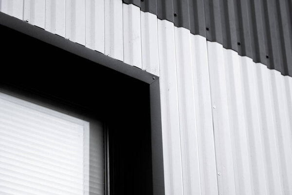 Black and white corrugated iron sheet used as a facade of a warehouse or factory with a window. Texture of a seamless corrugated zinc sheet metal aluminum facade. Architecture. Metal texture