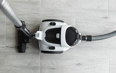 Gri bir fayansta torbasız hortum süpürgesi. Aspirasyon vasıtasıyla zeminden ve diğer yüzeylerden toz ve küçük parçacıkları toplayan elektrikli cihazlar..