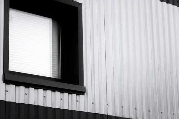 Black and white corrugated iron sheet used as a facade of a warehouse or factory with a window. Texture of a seamless corrugated zinc sheet metal aluminum facade. Architecture. Metal texture. — Stock Photo, Image