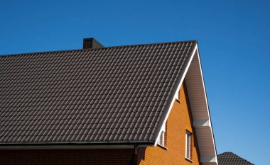 Modern bir eve kahverengi, metal profil çatısı döşenmiş. Çürük çarşafın çatısı. Metal profil dalgalı şeklinin çatısı. Metalden yapılmış modern çatı. Metal çatı..