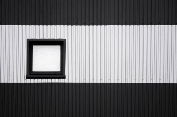 Black and white corrugated iron sheet used as a facade of a warehouse or factory with a window. Texture of a seamless corrugated zinc sheet metal aluminum facade. Architecture. Metal texture.