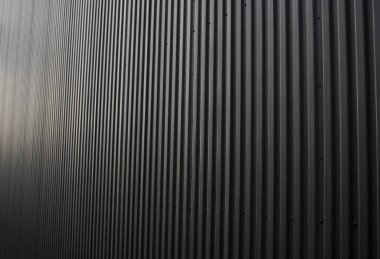 Bir depo ya da fabrika cephesi olarak kullanılan siyah kıvrımlı demir çarşaf. Sivri uçlu çinko kaplamalı metal alüminyum cephenin dokusu. Mimarlık. Metal doku.