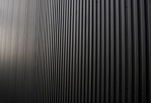 Black corrugated iron sheet used as a facade of a warehouse or factory. Texture of a seamless corrugated zinc sheet metal aluminum facade. Architecture. Metal texture.