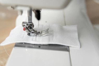 Tahta bir masanın üzerinde beyaz bir bez olan dikiş makinesi..