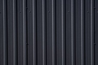 Bir depo ya da fabrika cephesi olarak kullanılan siyah kıvrımlı demir çarşaf. Sivri uçlu çinko kaplamalı metal alüminyum cephenin dokusu. Mimarlık. Metal doku.