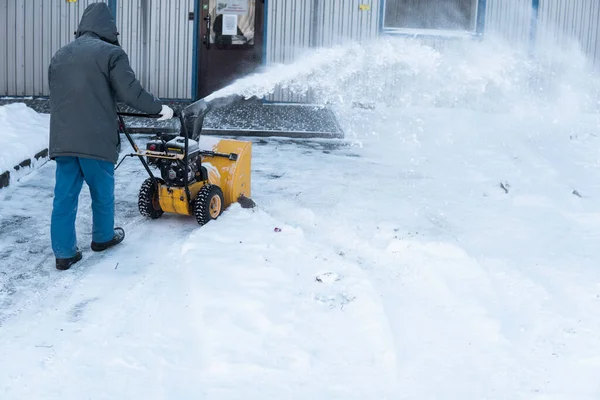 De man die de oprit schoonmaakt met sneeuwmachines na een sneeuwstorm. Sneeuwruimers werken op straat. Reiniging van straten tegen sneeuw. Het sneeuwt. — Stockfoto