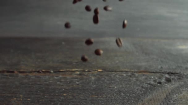 Los granos de café tostados frescos caen sobre una mesa de madera y rebotan. Café tostado fresco en granos de Arábica se prepara para moler y hacer delicioso café. — Vídeo de stock