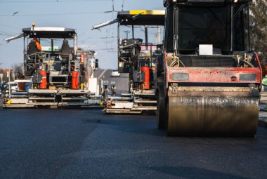 Şehir caddesinde güneş ışığında asfalt silindirli ve asfalt asfalt döşeyen yol şantiyesine yakın..
